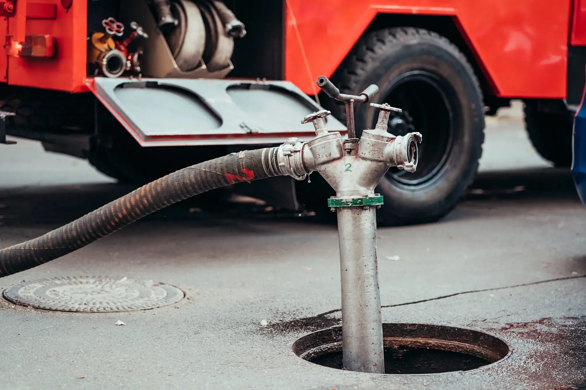 Fire hydrant connected to a thick hose with a red fire truck in the background.