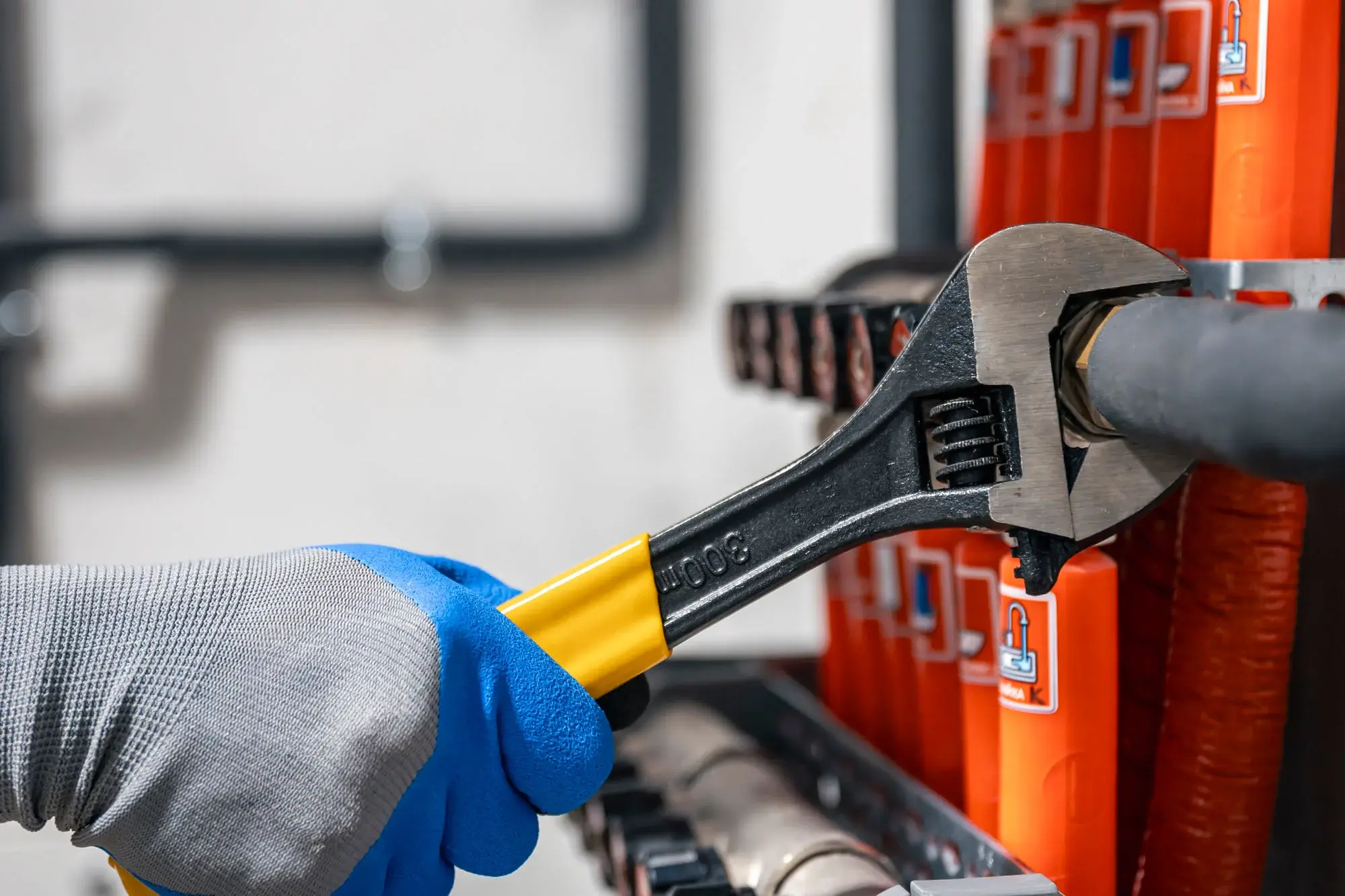 Gloved hand using a crimping tool on an orange shelving unit or rack in a workshop setting.